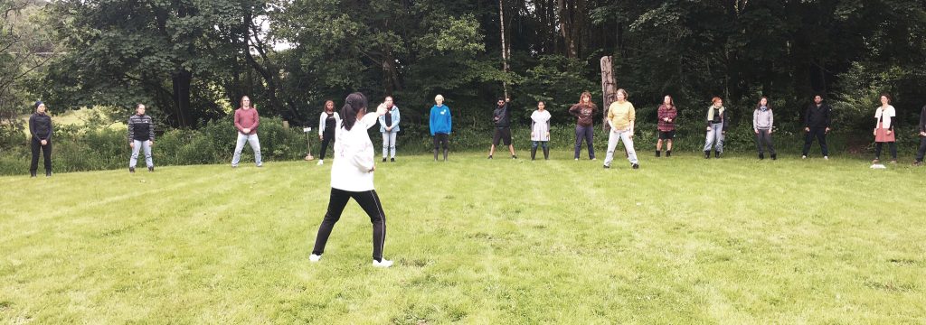 Nagako Cooper, with her back to the camera, demonstrating a Shintaido movement for participants to follow
