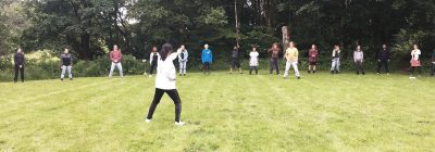 Nagako Cooper, with her back to the camera, demonstrating a Shintaido movement for participants to follow